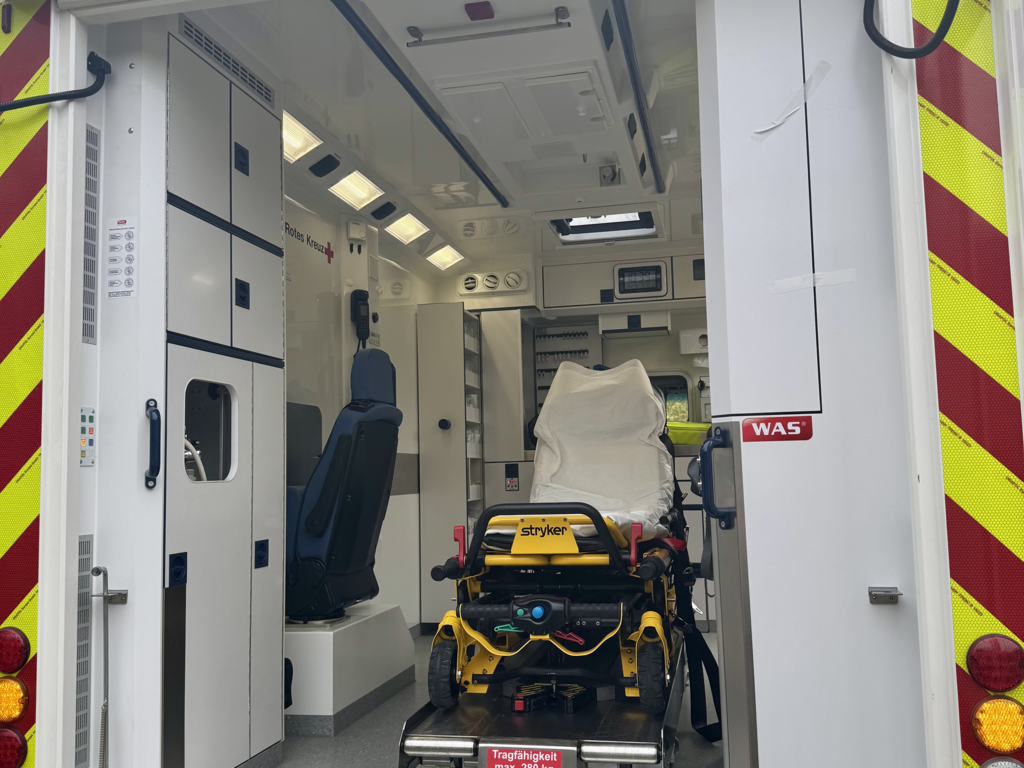Innenraum eines Rettungswagens mit einer gelben Trage auf einer Hebevorrichtung.